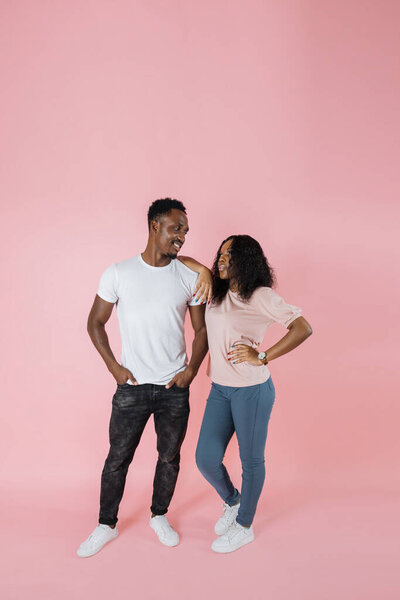 Full length view of stylish african american woman in casual outfit leaning on man standing with hands in pockets on pink background, copy space. 图片素材