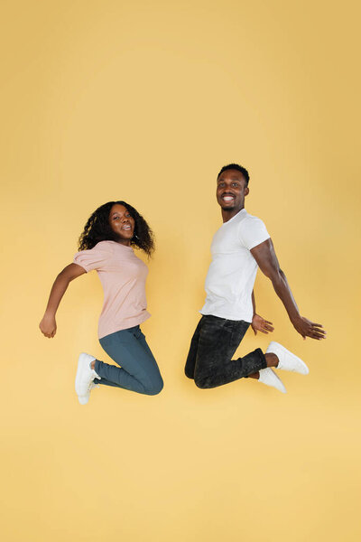 Full length shot of jumping african couple having fun together. Studio photo of young people on yellow background, copy space 图片素材