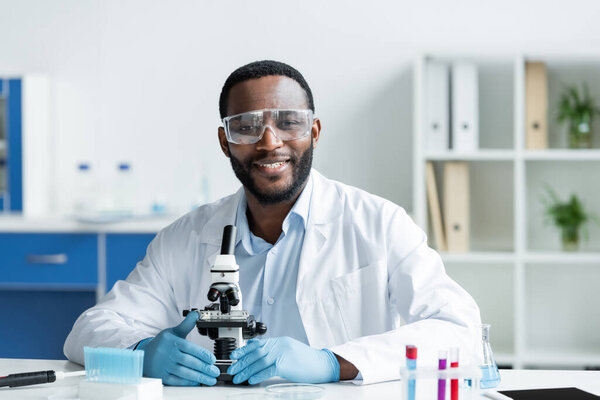 穿着护目镜在实验室显微镜下看着相机的非洲裔美国科学家  图片素材