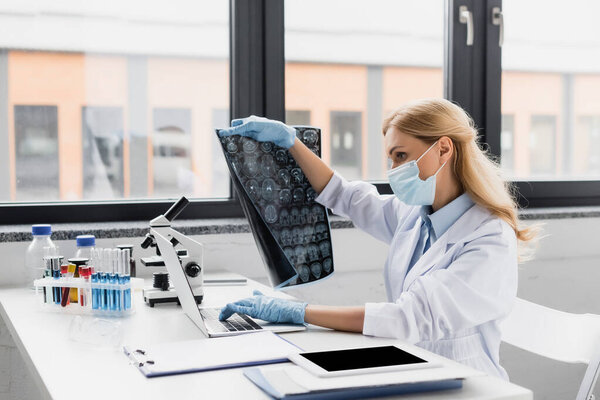 戴医疗面罩的科学家在桌子上的设备附近拿着X光 图片素材