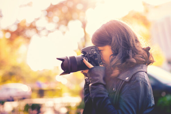 年轻漂亮的女人用专业数码相机外拍照的摄影师。老式的影响