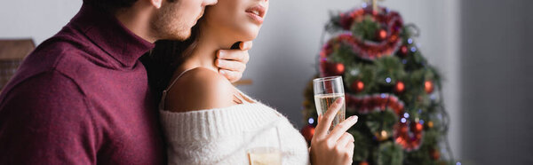照片上，充满热情的男人亲吻着女人，带着香槟酒在模糊的背景下，挂着横幅的圣诞树旁举杯 图片素材