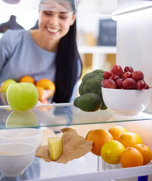 微笑的女人从冰箱里拿出新鲜的水果，健康的食物概念 图片素材