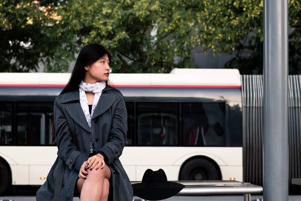 亚洲妇女坐在那里等公共汽车，等公共汽车站，公共交通的概念和城市生活方式 图片素材