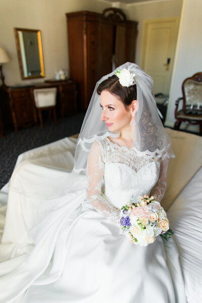 美丽年轻的新娘化妆、 花式发型在白色的连衣裙和纱坐在床上展望 图片素材