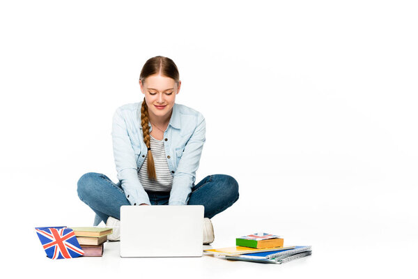 笑着的女孩坐在地板上，用笔记本电脑靠近书本和复印机，英国国旗与白色隔离 图片素材