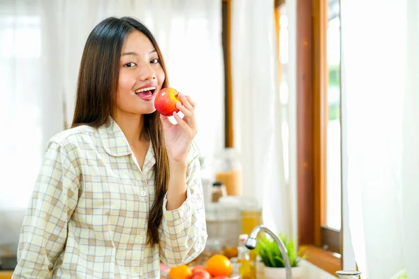 亚洲漂亮的少女在厨房里吃着红苹果. 图片素材