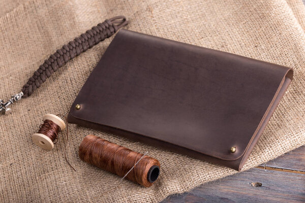 皮革深色棕色钱包在一个黑暗的木质背景, 与线程和针. 图片素材