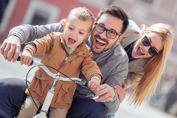 父亲和母亲教他们的儿子在城市骑自行车在晴朗的天. 图片素材