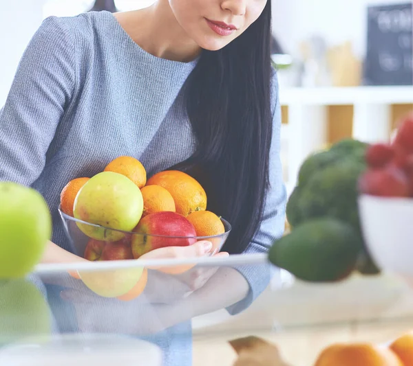 微笑的女人从冰箱里拿出新鲜的水果，健康的食物概念 图片素材