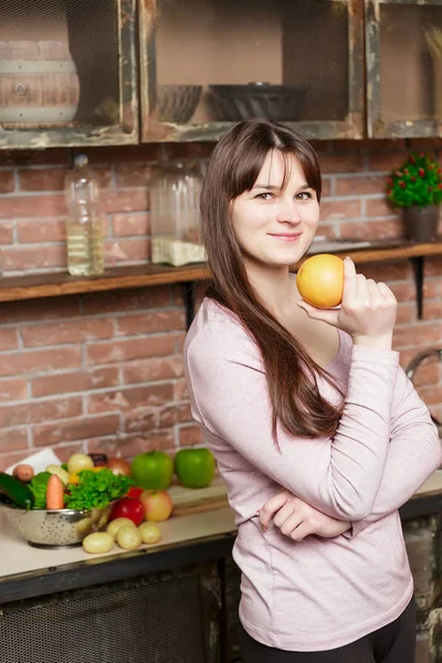 女人她手里拿着一个橘子。年轻的女人在家里的厨房里做饭。健康的食物。饮食. 图片素材