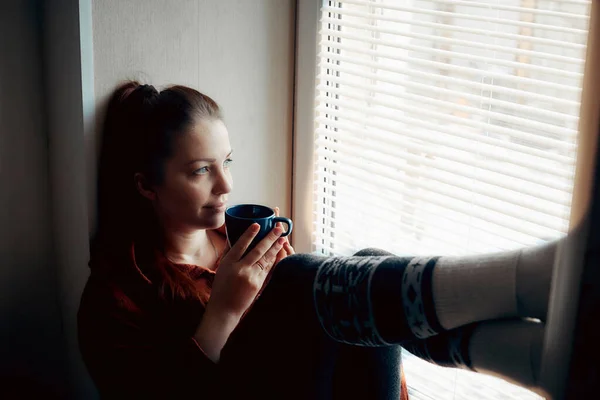 一个年轻的女人坐在窗边, 拿着一杯热茶 图片素材