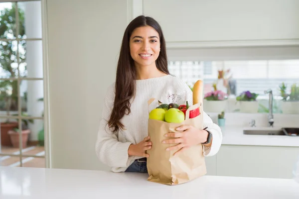 美丽的年轻女子微笑着拿着一个纸袋装满杂货在厨房 图片素材
