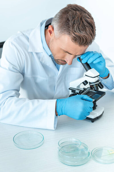 英俊的科学家用显微镜在白色隔离测试 图片素材