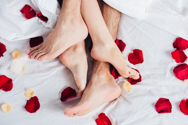 部分看法赤脚夫妇躺在柔软的白色床上用品与红色花瓣  图片素材