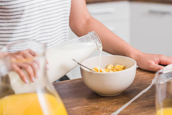 在厨房早餐期间, 女孩用玉米片将牛奶从瓶子倒入盘子中的图像 图片素材