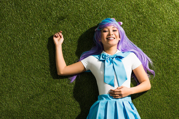 微笑的亚洲动漫女孩在紫色假发躺在绿草 图片素材