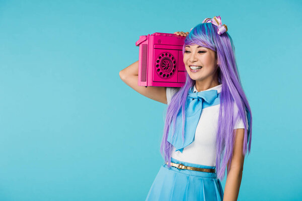 微笑的亚洲宅男女孩在紫色假发拿着动臂盒孤立在蓝色 图片素材
