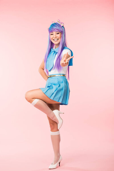 快乐的亚洲动漫女孩站在一条腿上，在粉红色上显示和平标志的全长视图 图片素材