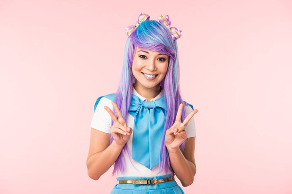 快乐的亚洲动漫女孩在紫色假发显示和平标志孤立在粉红色 图片素材