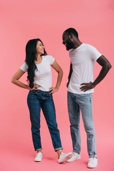 笑年轻的非洲裔美国人夫妇双手在腰上看着彼此孤立的粉红色背景  图片素材