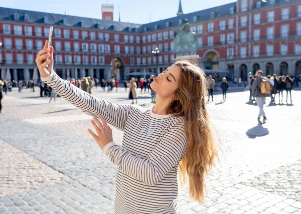 美丽的年轻高加索学生旅游妇女采取自拍或视频为她的旅游和周游世界博客网络在西班牙市长广场。在欧洲的社交媒体和度假. 图片素材