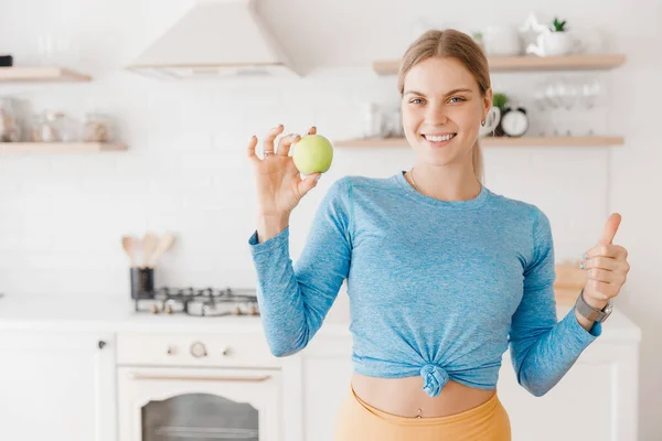 美丽的白种人运动女人快乐地微笑着，在厨房里拿着健康的绿色苹果 图片素材