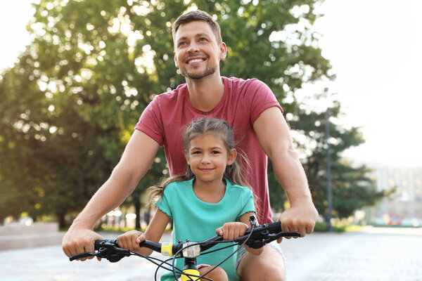 快乐的父亲与女儿骑自行车在城市 图片素材