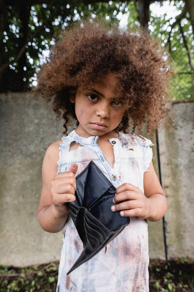 非洲裔美国儿童穿着肮脏衣服，手里拿着空皮夹，看着城市街道上的相机，有选择地聚焦在他们身上  图片素材