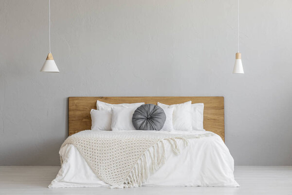 在木床上的针织毯子, 在最小的卧室内部与灯的灰色墙壁。真正的照片与一个地方为您的床头柜 图片素材