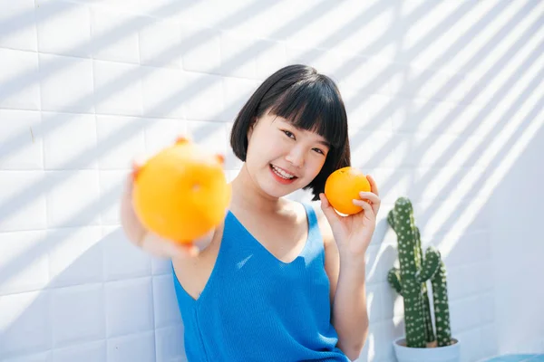 健康的胖胖的美发亚洲女人，身穿蓝色背心，双手托着两个橙子，盖在白色背景上. 图片素材