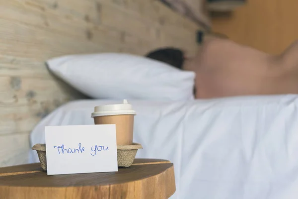 一杯纸杯咖啡和贴纸，上面写着"谢谢"，站在卧室的桌子上，给熟睡的女孩一个惊喜.  图片素材