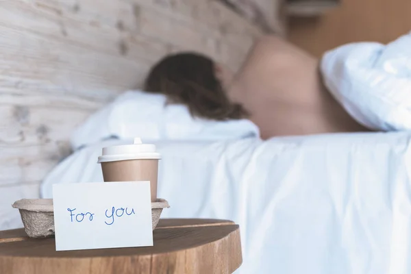 一杯纸杯咖啡和贴纸，上面写着"为你"，站在卧室的桌子上，给一个熟睡的女孩一个惊喜.  图片素材