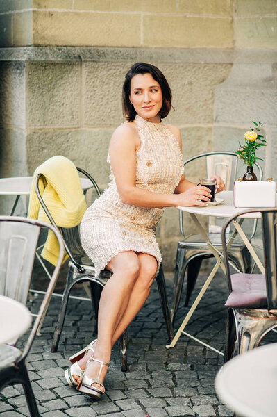 美丽的时尚女人在街头咖啡馆休息，一杯咖啡，穿着时髦的礼服 图片素材