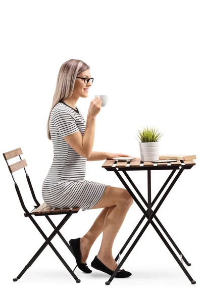 一个年轻女子喝咖啡, 坐在一张桌子上被隔离的白色背景的全长轮廓照片 图片素材