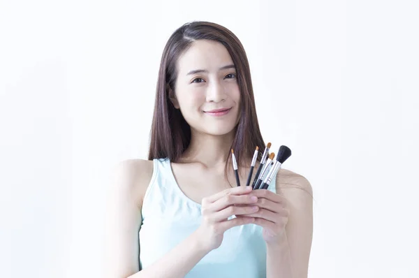 年轻的亚洲妇女拿着一些化妆工具, 对着镜头微笑 图片素材