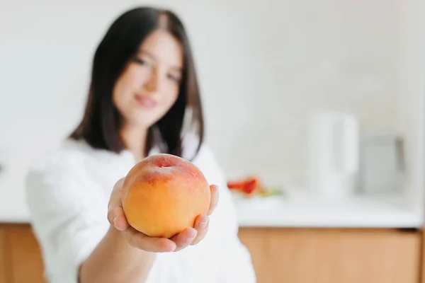 成熟的桃子在女人的手背现代的白色厨房。新鲜的夏季水果，健康的食物概念。家庭烹饪 图片素材