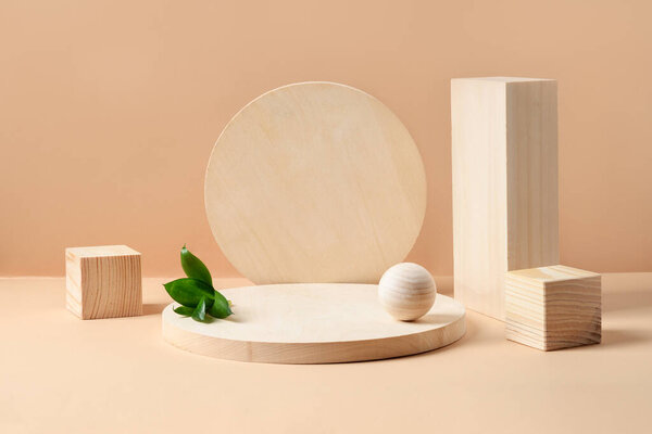 木制天然材料产品的立柱。方块、球和盘子作为货物的讲台.米色背景的绿叶成分. 图片素材