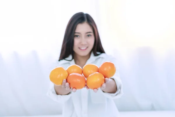 生活方式和健康食品的概念。将手中拿着新鲜橙子的年轻女子的双手集中在家里的白色床上，并留有复制的空间。柑橘类水果. 图片素材