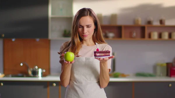 Woman choosing between cake and apple on kitchen. Woman choosing cake 图片素材