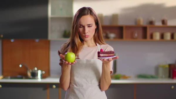 Woman making choice between apple and cake on kitchen. Woman choosing apple 图片素材